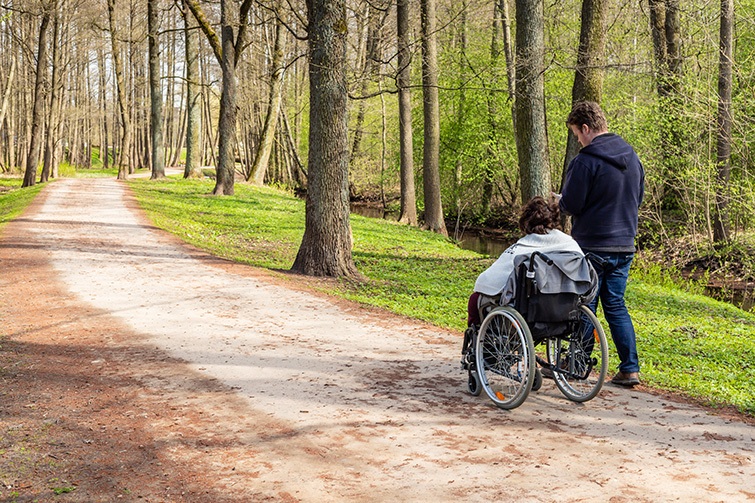 Person i rullstol tillsammans med personlig assistent i skogen.