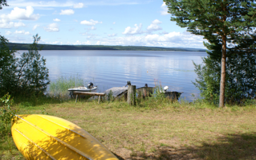 En gul kanot ligger upp och ner på land. Två ekor med motor vid bryggan.
