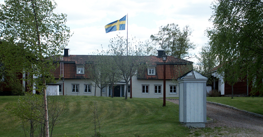 En herrgårdsbyggnad med stor gräsmatta framför. Flaggan är hissad.