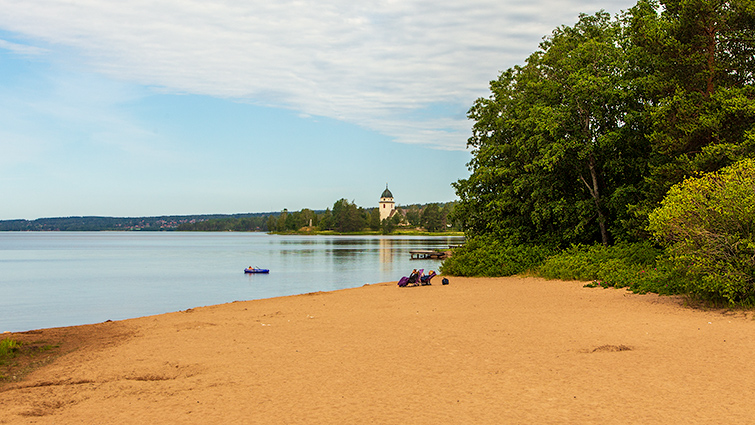 Två personer på Siljans strand och ett barn i båt en tidig sommarmorgon. 
