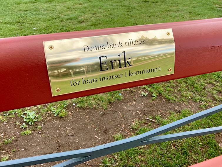 Bänkens plakett  där texten "Denna bänk tilläras Erik för hans insatser i kommunen" är inristad.