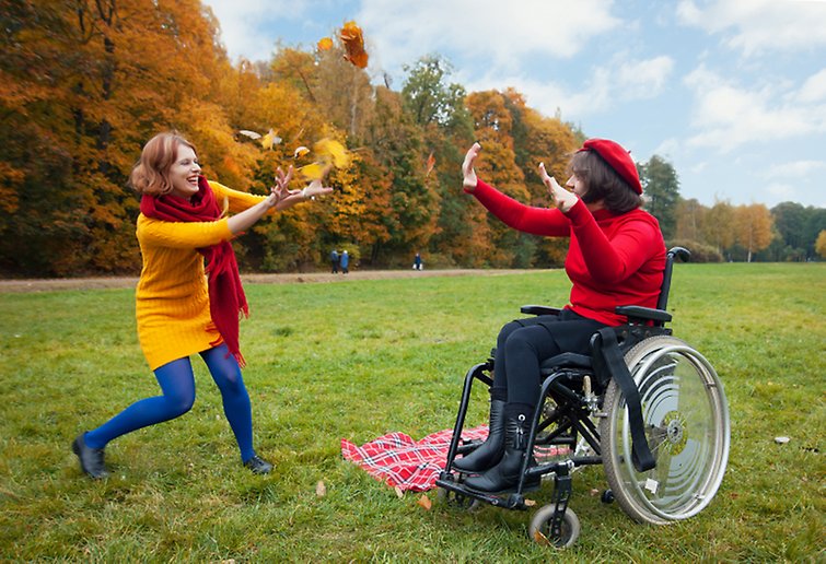 Två kvinnor leker, den ena sitter i rullstol.