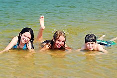 Tre barn som ligger i vattnet i en sjö.